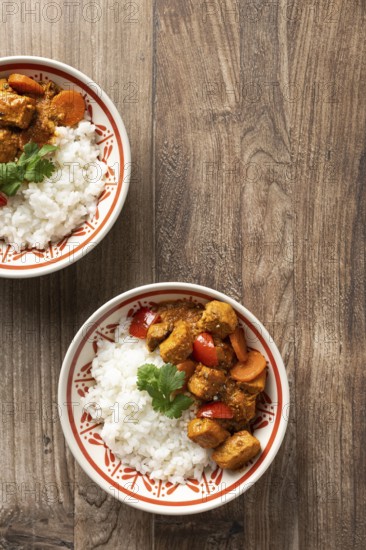 From above, two bowls of Hungarian pork goulash served with rice, garnished with a parsley leaf on a wooden surface. The dish features chunks of pork, carrots, and tomatoes in a savory sauce
