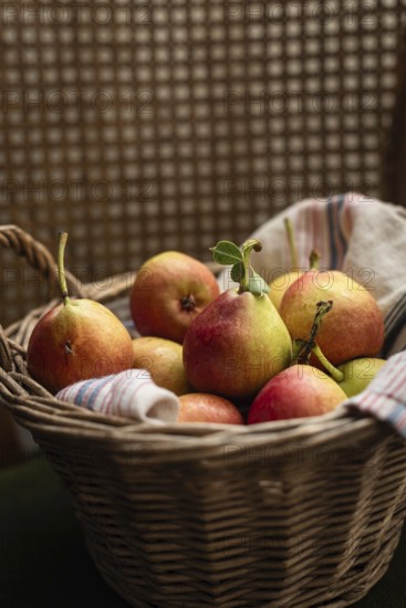 A charming wicker basket filled with ripe pears, resting on a striped textile. The warm tones and soft texture create a cozy, rustic ambiance perfect for country themed decor