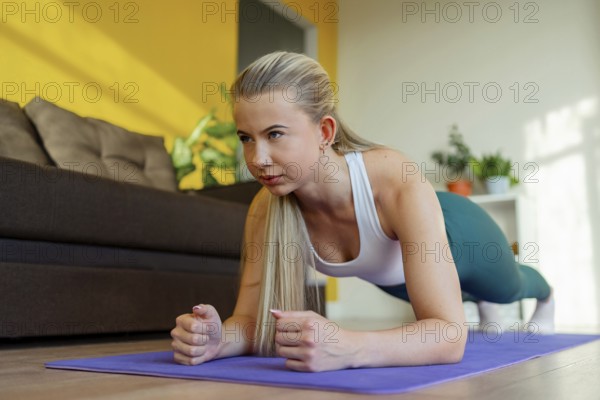 A woman performing a plank exercise on a yoga mat in her living room. Focused on core strength and fitness, surrounded by a comfortable and bright home setting