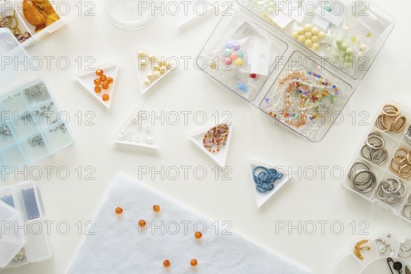 Top view of a jewelry making studio setup featuring various beads and rings in organized containers. Essential materials for crafting handmade jewelry and accessories