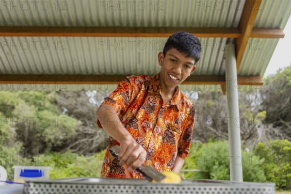 An Indonesian individual showcases vibrant batik clothing while cooking outdoors in Australia. The harmonious blend of culture and nature highlights the beauty of diversity