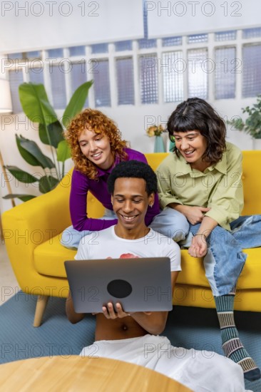 Vertical photo of three multiracial Lgtb people using laptop sitting together in a modern sofa
