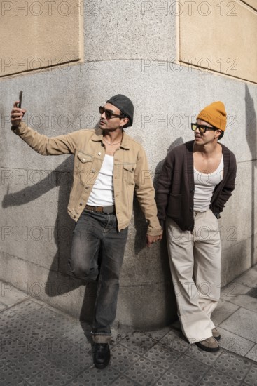 A Colombian couple taking a selfie, hand in hand. They lean against a city wall, embodying modern fashion and companionship. One takes a selfie, capturing the moment