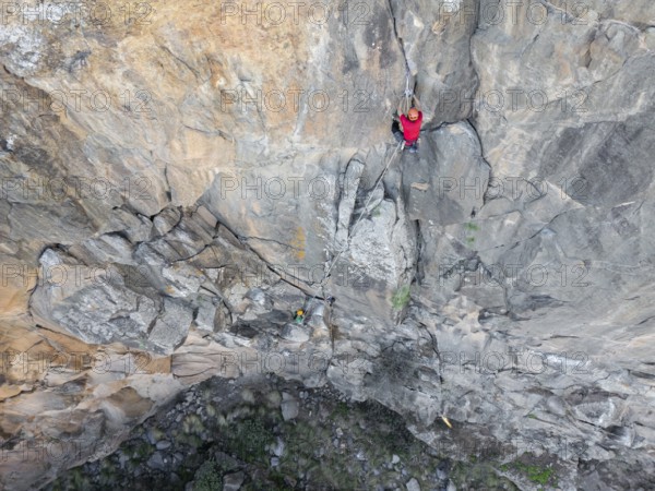 Two climbers in red gear expertly scales a rugged rock face using traditional climbing techniques. The breathtaking view highlights the raw beauty of nature and adventure