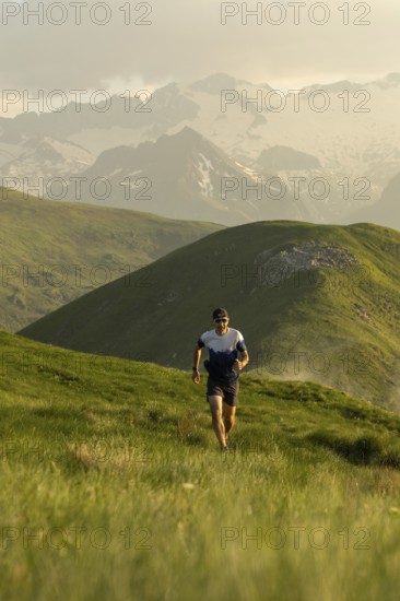 A lone runner navigates a picturesque trail through vibrant green mountains, wearing a hat and sunglasses under a cloudy sky, embodying the spirit of outdoor adventure