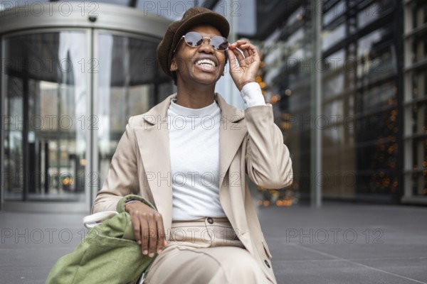 A stylish black woman smiles confidently in an urban setting She wears chic sunglasses and a fashionable hat, embodying modern city life The background is sleek and contemporary