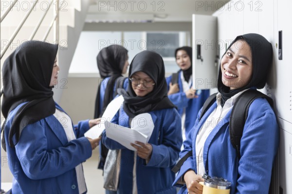 Asian Muslim students in hijabs and uniforms gather in a bright school hallway, engaging with each other and holding educational materials, showcasing the back to school spirit