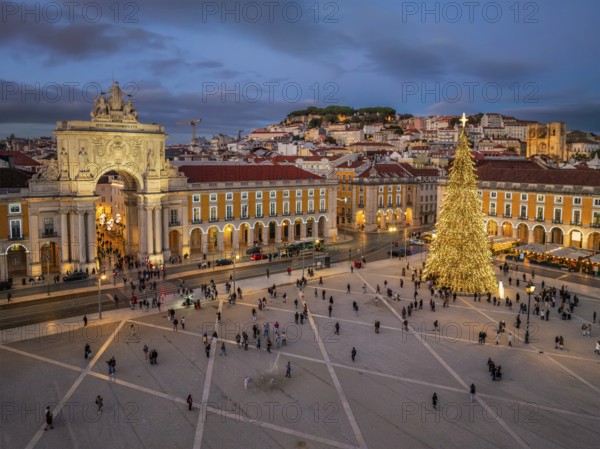 Twilight lights up Praca do Comercio, where a grand Christmas tree and festive displays fill the air with holiday cheer. Lisbon, Portugal