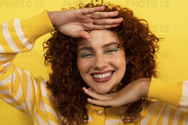 A joyful woman with curly hair looking at camera, smiles brightly against a vivid yellow background. She wears a striped sweater, exuding warmth and happiness, incorporating dynamic, cheerful energy