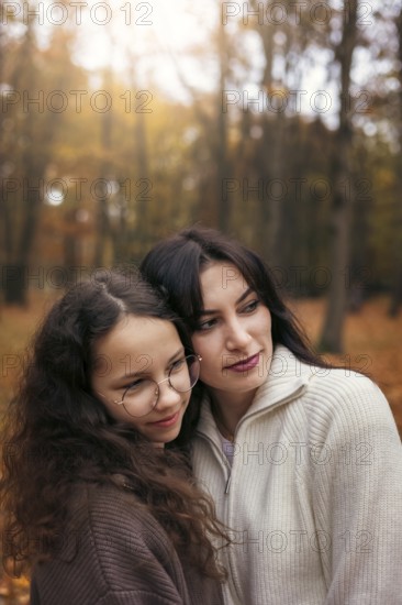 A warm embrace between a mother and daughter amidst the golden autumn foliage, capturing a tender family moment in nature. Both wear cozy sweaters, reflecting autumn coziness
