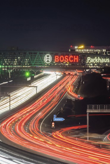 A8 motorway at Stuttgart Airport in the evening. Heavy traffic, lanes of light. Modern architecture of Messe Stuttgart with multi-storey car park above the motorway lanes. Logo of the Bosch company. Stuttgart, Baden-Württemberg, Germany