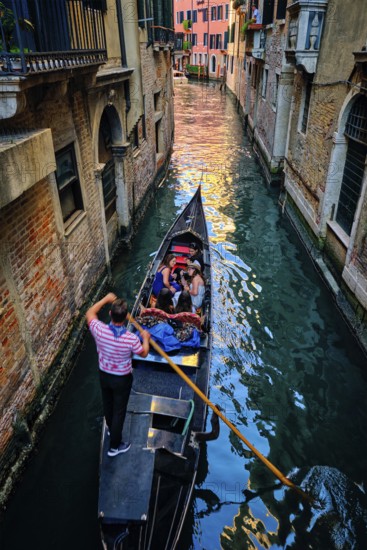VENICE, ITALY, JUNE 27, 2018: Narrow canal between colorful old houses with gondola boat with tourists and gonolier in Venice, Italy