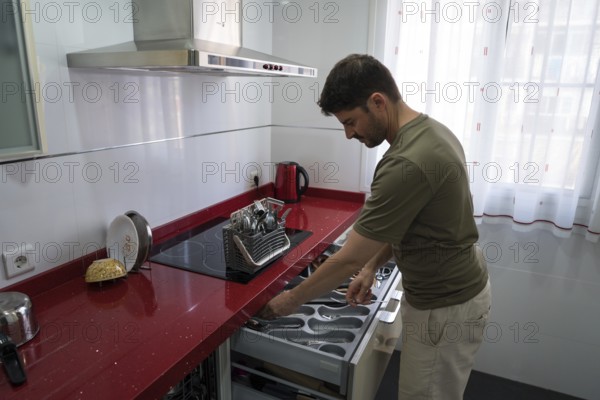 A man is organizing utensils in a modern kitchen. He carefully arranges cutlery in a drawer, demonstrating efficient household management and attention to detail