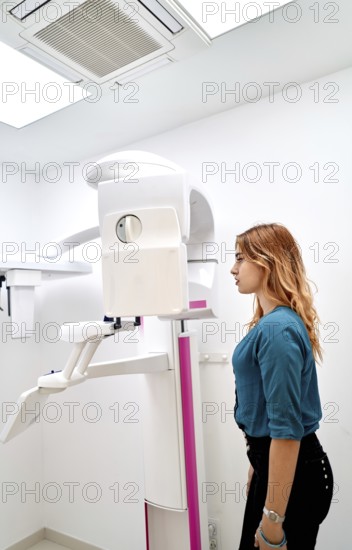 A young woman stands in a dental clinic, preparing for a panoramic dental X-ray. The advanced imaging machine ensures accurate diagnostics and effective dental care