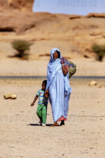 Mother and child in traditional dress walk together through a barren, sandy desert, woman in the Sahara in Algeria