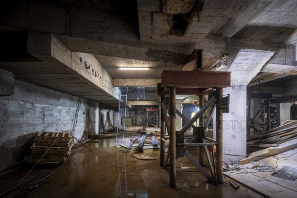 A dimly lit basement under construction, with structural beams and tools scattered about. The work shows progress and potential, highlighting the intricate details of the building's development