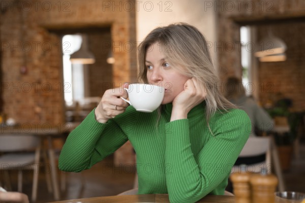 Woman enjoys a relaxing morning at a cozy cafe, sipping coffee. The warm interior ambiance adds to the peaceful breakfast experience