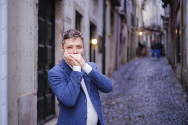 Man musician in a blue blazer and white sweater playing blues on a harmonica with eyes closed, standing outdoors in Lisbon city street, Portugal