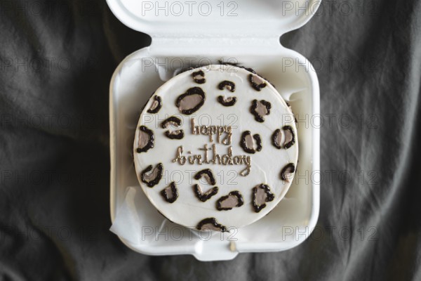 Top view of a stylish bento birthday cake with happy birthday message, neatly presented in a white takeout box against a textured gray background