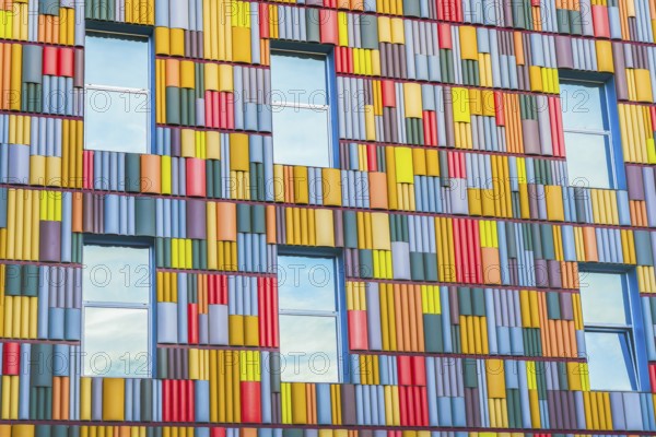 A detailed view of a building facade covered in a multitude of brightly colored panels arranged in a geometric pattern, highlighting modern architectural design elements