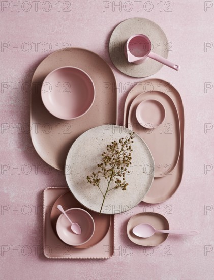 Top view of an artistic arrangement of ceramic crockery, featuring various shades of pink and rustic textures. A delicate dried flower complements the smooth and matte finishes