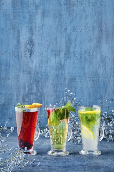 Three glasses with hot fruit and herbal tea on blue background