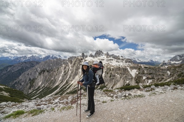 A smiling mother with her baby in a carrier hikes through the breathtaking snow-capped peaks of Tre Cime di Lavaredo in the Dolomites, Italy. A moment of adventure, bonding, and natureâ€™s beauty