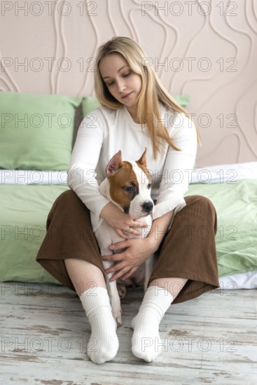 A woman sits comfortably in a home setting, gently holding and looking at a young dog in her arms. The image evokes feelings of love and companionship
