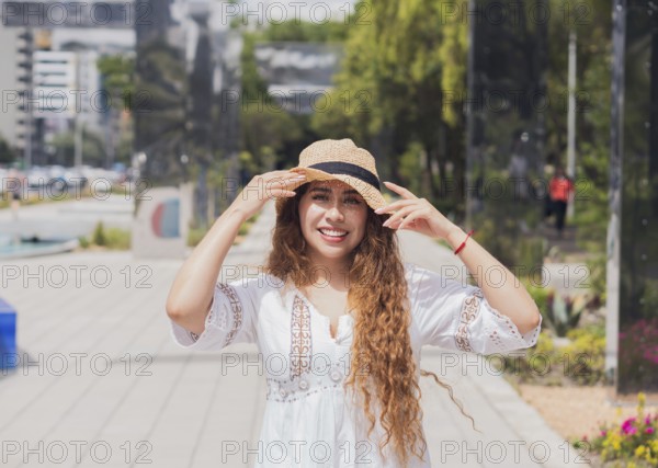 Young American Latin woman in a casual white dress and straw hat, smiling brightly in an urban park. Embracing joyful moments, reflecting a vibrant lifestyle
