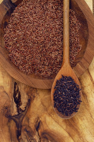 Red and black rice, in a wooden bowl and spoon on a wooden surface in rustic style, top view