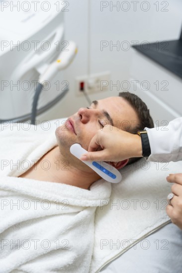 Man receiving modern facial treatment with a handheld device at an aesthetic clinic, focused on skincare, wellness and anti aging in a clean, professional medical spa setting