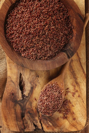 Natural, red rice, in a wooden bowl and spoon on a wooden surface in rustic style, top view