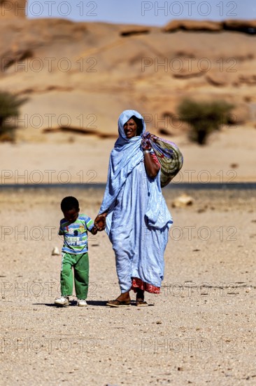 Mother and child, both in traditional dress, walking through a barren desert landscape, woman in the Sahara in Algeria