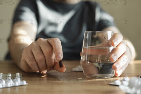Man sits at a table, holding a pill in one hand and a glass of water in the other. The scene captures a moment of taking medication at home, emphasizing wellness and self-care