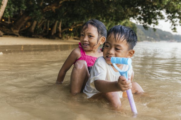 Two cheerful children enjoy playing in the shallow waters of a Philippine beach, with laughter and smiles, while one holds a colorful toy on a bright sunny day