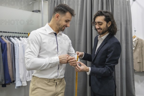 A tailor measures a customer for a custom suit in a suit store. The scene captures precision and professionalism in tailoring, with a range of suits displayed