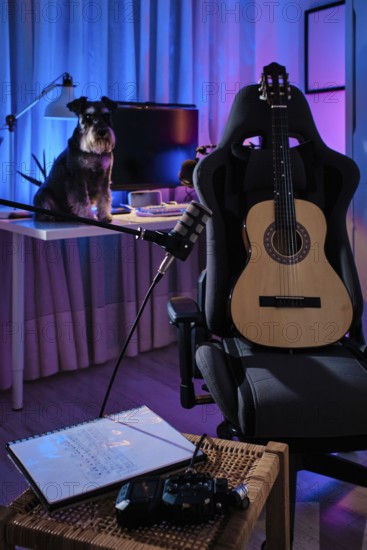 A cozy home studio with a guitar on a chair, a dog on the desk, and ambient purple and blue lighting. A microphone and notebook enhance the creative atmosphere