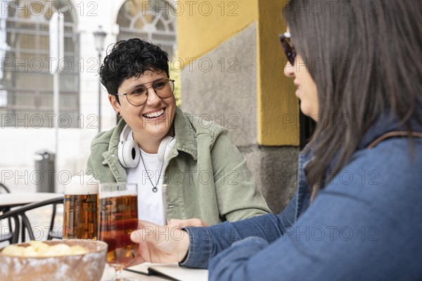 A joyful scene of a curvy lesbian couple enjoying beers at a bar. They appear relaxed and happy, sharing a moment of laughter and connection
