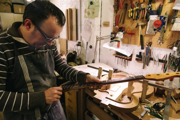 A luthier meticulously crafts a bass guitar neck in a workshop filled with tools. The focus is on precision and craftsmanship, showcasing a personal touch in instrument making