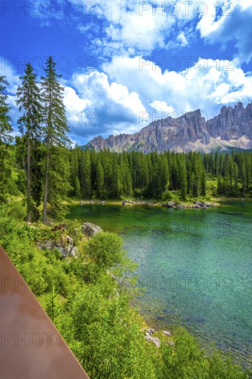 Emerald waters of lake carezza reflecting latemar mountain range in dolomites on a beautiful sunny summer day, italian alps