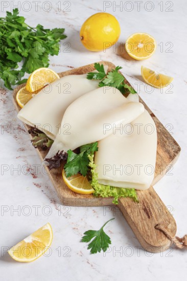 Fresh squid prepared for cooking, surrounded by herbs and lemon, placed on a wooden chopping board in a bright kitchen setting