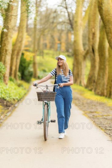 Happy young woman walking with her vintage bicycle in a park, enjoying a sunny day of leisure