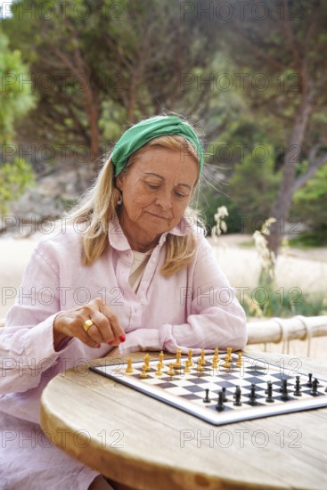 A senior woman plays chess outdoors, deeply focused on her strategic moves The serene natural setting adds a peaceful backdrop to this intellectual pursuit