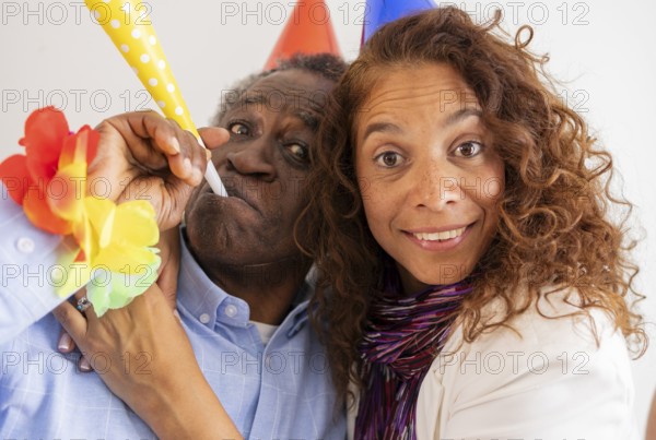 A joyful moment at a birthday celebration featuring two people wearing colorful party hats and leis, with one using a vibrant noise maker. The scene captures excitement and festivity