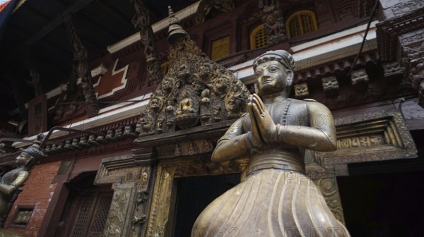 Statue of a praying figure in traditional dress against an ornate temple background, Kathmandu, Nepal