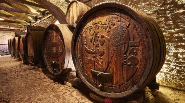 Row of wooden barrels with ornate engravings in a rustic wine cellar, Achaia Clauss Winery, Patras, Peloponnese, Greece