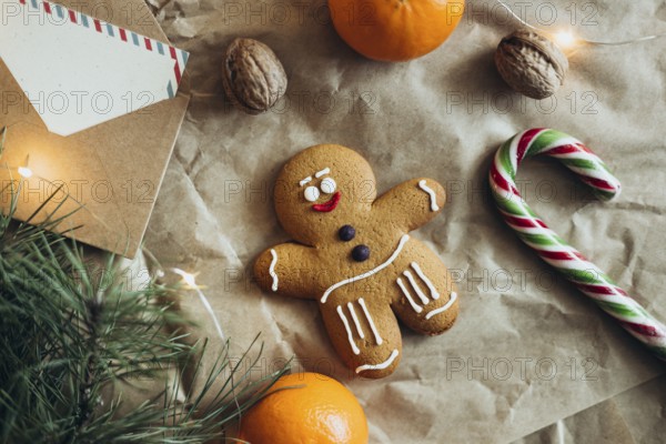 A charming gingerbread man cookie surrounded by holiday elements like a candy cane, nuts, tangerine, pine branches, and twinkling lights, invoking Christmas spirit