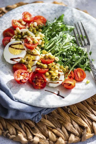 A vibrant keto lunch featuring boiled eggs, fresh rocket leaves, cherry tomatoes, canned green peas, and sprouted green beans, all dressed with balsamic sauce