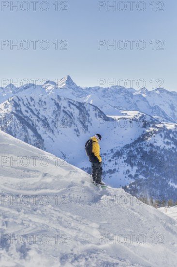 A snowboarder in a yellow jacket enjoys the snowy slopes with stunning mountain views. Bright sunlight and clear blue sky add to the winter wonderland experience