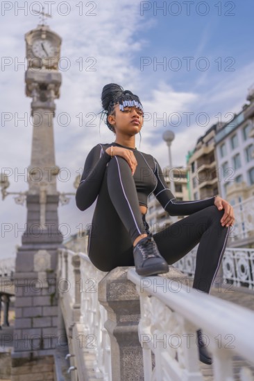 Beautiful Dominican Ethnic Girl with with braids with full body suit. Fashion, sitting on the beach railing in summer